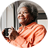 Woman in orange shirt holding a mug and smiling at a window