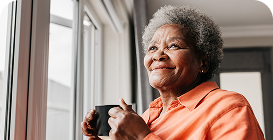 Woman in orange shirt holding a mug and smiling at a window
